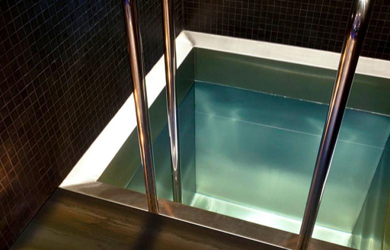 A small, square stainless steel cold plunge pool with handrails to aid entry and exit
