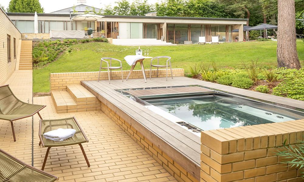 Outdoor stainless steel hot tub pool set in a private garden, surrounded by a wall and patio.