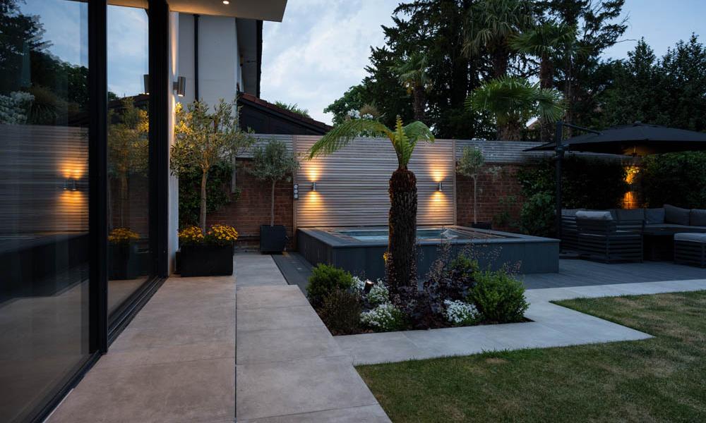 Stainless steel hot tub set discreetly into private landscaped garden at dusk.