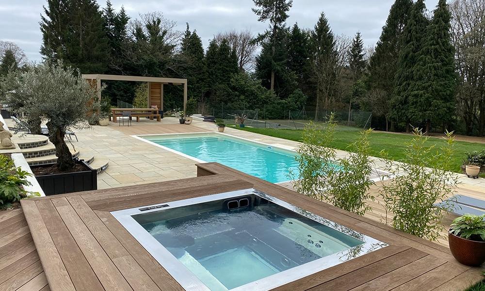 spaflo completed hot tub installation - stainless steel set within decking in a private decking with a swimming pool in the background