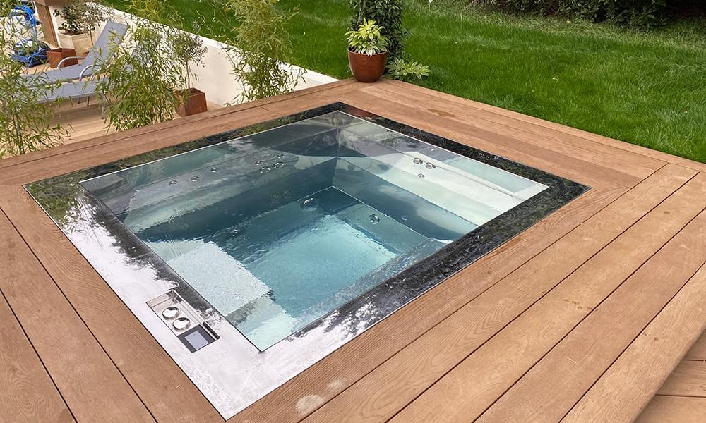 luxury stainless steel hot tub completed installation - set within wooden decking in private garden - sun loungers in background