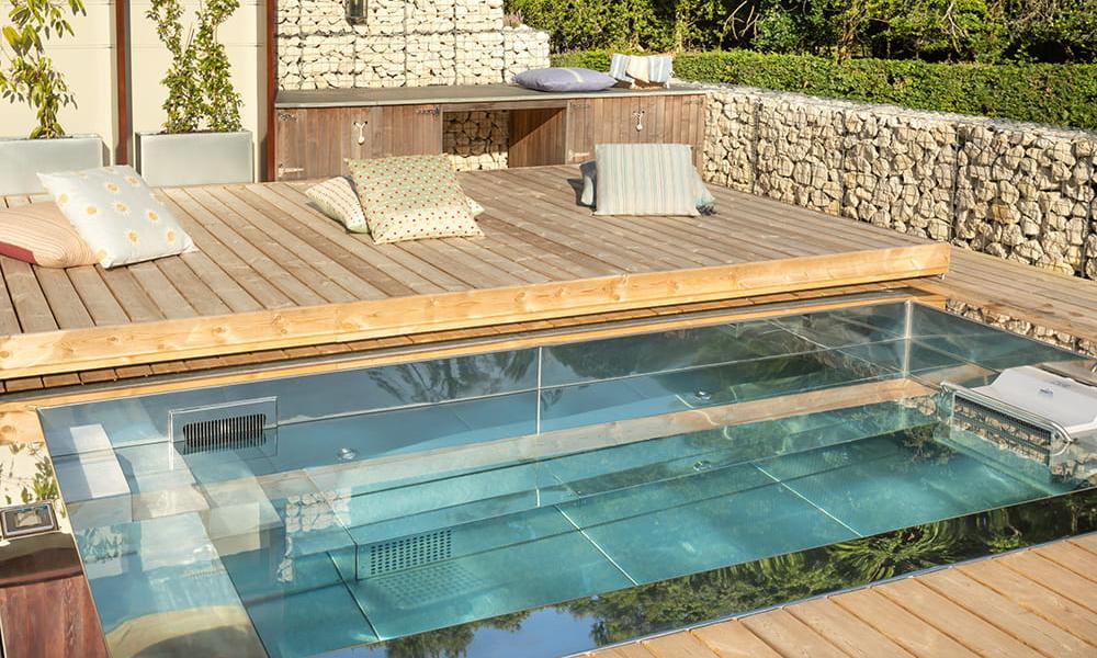 Bespoke stainless steel swimming pool set in the ground in a luxury outdoor space surrounded by decking and gabion basket stone walls